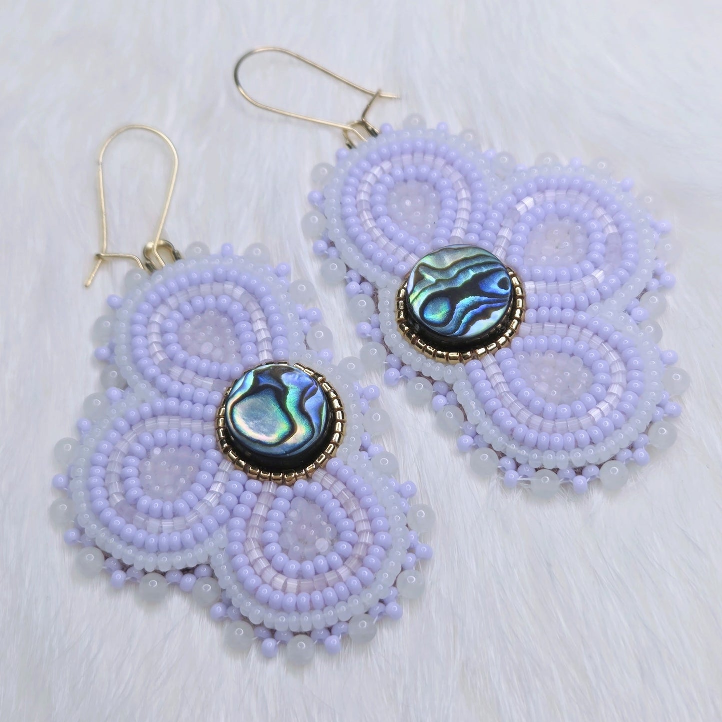 Pair of beaded earrings with abalone shell centers on a light background