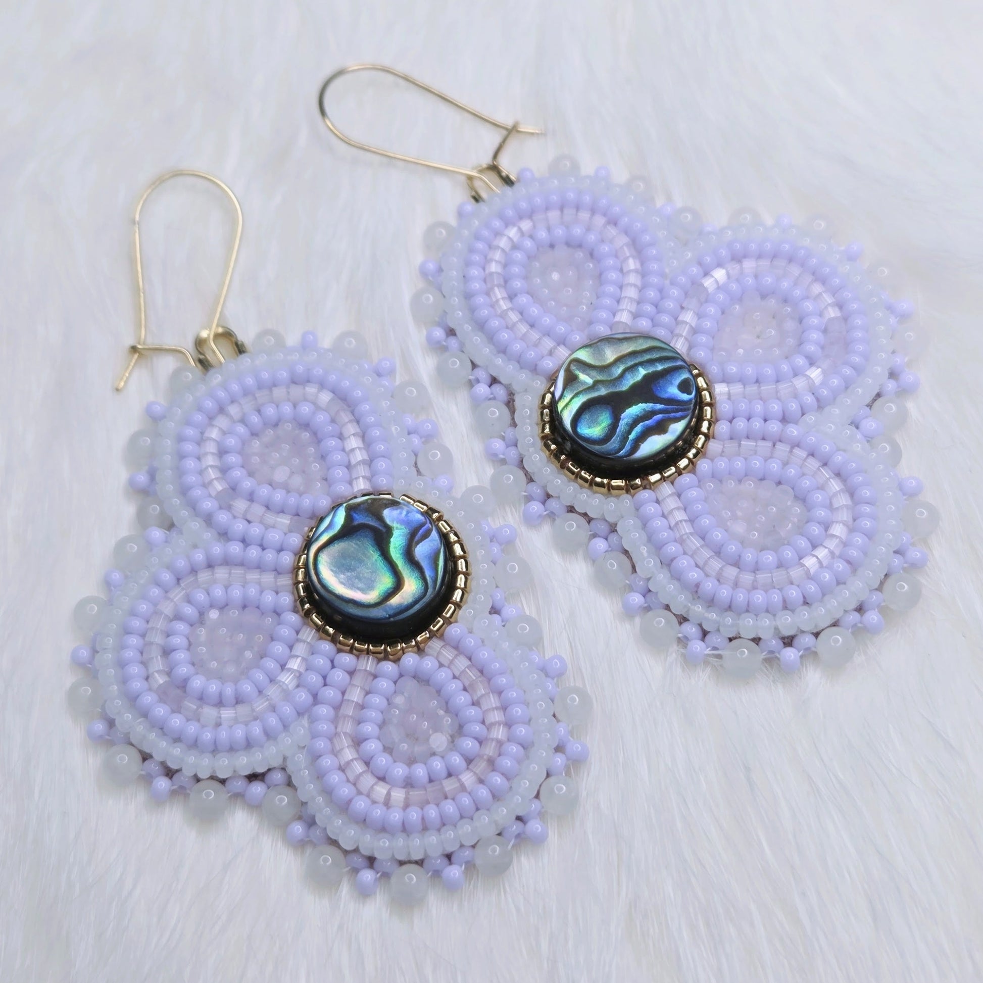 Pair of beaded earrings with abalone shell centers on a light background